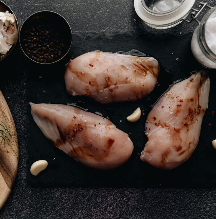 A cutting board with three chicken breasts and garlic.